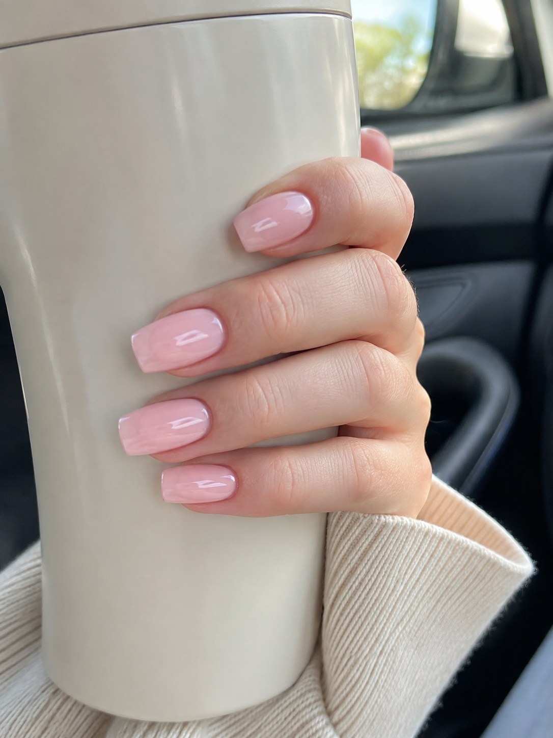 Hand holding a tumbler showing milky pink coffin nails short with a glass-like glossy finish