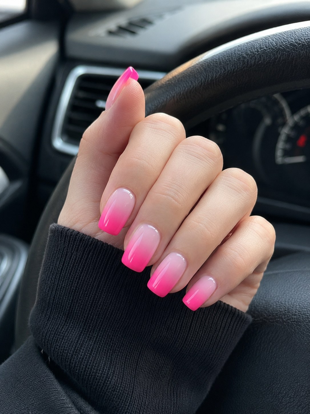 Hand on a steering wheel showing bold magenta-to-white ombré coffin nails short