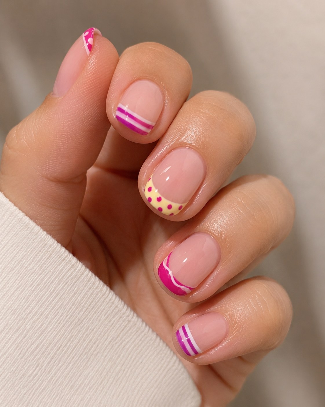 Bright pink and yellow short french tip nails with polka dots and stripes for a birthday mani